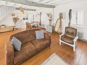 A spacious living area with a brown sofa, a white armchair, a dining table, and a staircase. - House with pool 50 m from Lascaux IV for four (Montignac)