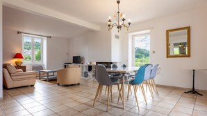 Een ruime woonkamer met een eettafel, stoelen, een bank, een televisie en een kroonluchter.
