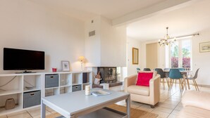 Een moderne woonkamer met een flatscreen televisie, een salontafel, een bank, een open haard en een eethoek met stoelen en een tafel.