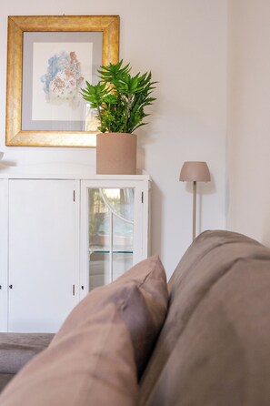 Ein Zimmer mit einer Couch, einem Schrank mit Glastüren, einem gerahmten Kunstwerk und einer Topfpflanze.