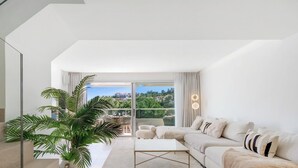 A modern living room with a sofa, coffee table, and large windows overlooking a cityscape. - The Don | Terrace - Views - Pool (La Cala de Mijas)