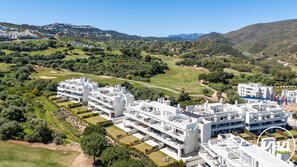 Un immeuble résidentiel moderne à plusieurs étages, doté d’une terrasse sur le toit, entouré d’une végétation luxuriante et d’un parcours de golf.
