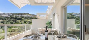 Un balcon avec une table dressée pour le dîner, une bouteille de vin et une vue sur une colline parsemée de bâtiments.