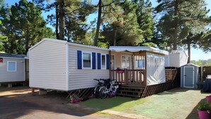 A mobile home with a porch, a bicycle, and a small shed. - Lovely mobile home for rent in st jean de monts for an unforgettable vacation (Saint-Jean-de-Monts)