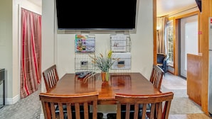 Een eetgedeelte met een houten tafel, stoelen, een flatscreen televisie en een plant als decoratie.