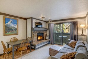 Ein gemütlicher Wohnbereich mit Kamin aus Stein, einem Esstisch mit Stühlen, einer Couch und Blick durch eine Glastür.