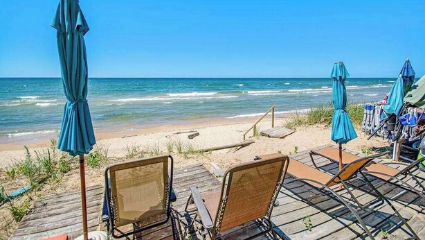 A beachside view with wooden deck chairs and umbrellas, a sandy beach, and the ocean. - Dog-friendly home with lake views, wood stove, kayaks/SUPs, & W/D (Coloma)