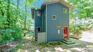 A small, single-story building with a red door, a small window, and a wooden staircase leading to a porch. - Dog-friendly home with lake views, wood stove, kayaks/SUPs, & W/D (Coloma)