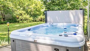Ein Whirlpool mit geöffnetem Deckel, umgeben von einem Rasen und Bäumen.