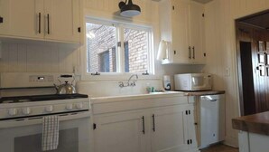A kitchen with white cabinets, a stove, a microwave, and a window with a view of a brick building.