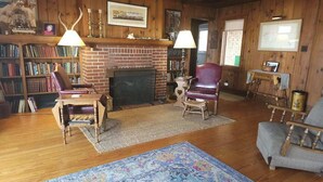 A cozy living room with a fireplace, wooden bookshelves, leather chairs, and a blue patterned rug.