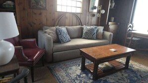 A living room with a sofa, patterned pillows, a wooden coffee table, a red chair, and a lamp.