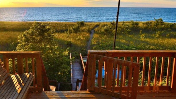 A wooden deck with a view of the ocean and a grassy path leading to a dock.