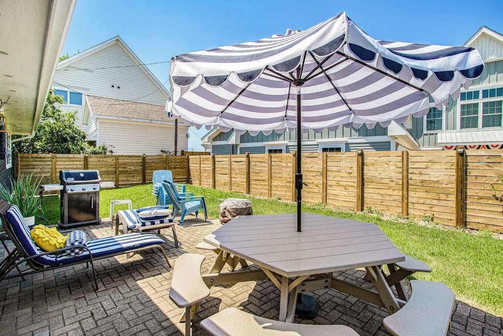 Een achtertuin met terras, een tafel, stoelen, een barbecue en een gestreepte parasol.