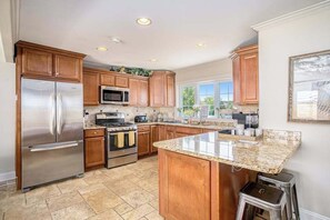 A kitchen with wooden cabinets, stainless steel appliances, granite countertops, and a large window. - Remodeled Home close to Lake Michigan - Walk to the Beach, One Dog OK (New Buffalo)