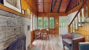 A wooden interior with a stone fireplace, wooden dining table, and a staircase. - Cute Cottage by the Lake W/ Private Hot Tub, Firepit, Screened Porch & Fast WiFi (Michiana)