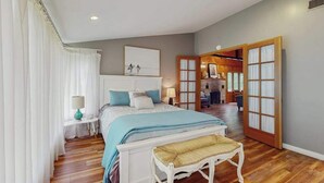 A bedroom with a bed, bedside tables, a bench, and a view into another room. - Cute Cottage by the Lake W/ Private Hot Tub, Firepit, Screened Porch & Fast WiFi (Michiana)