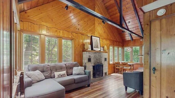 A cozy cabin interior with a fireplace, wooden floors, and large windows. - Cute Cottage by the Lake W/ Private Hot Tub, Firepit, Screened Porch & Fast WiFi (Michiana)