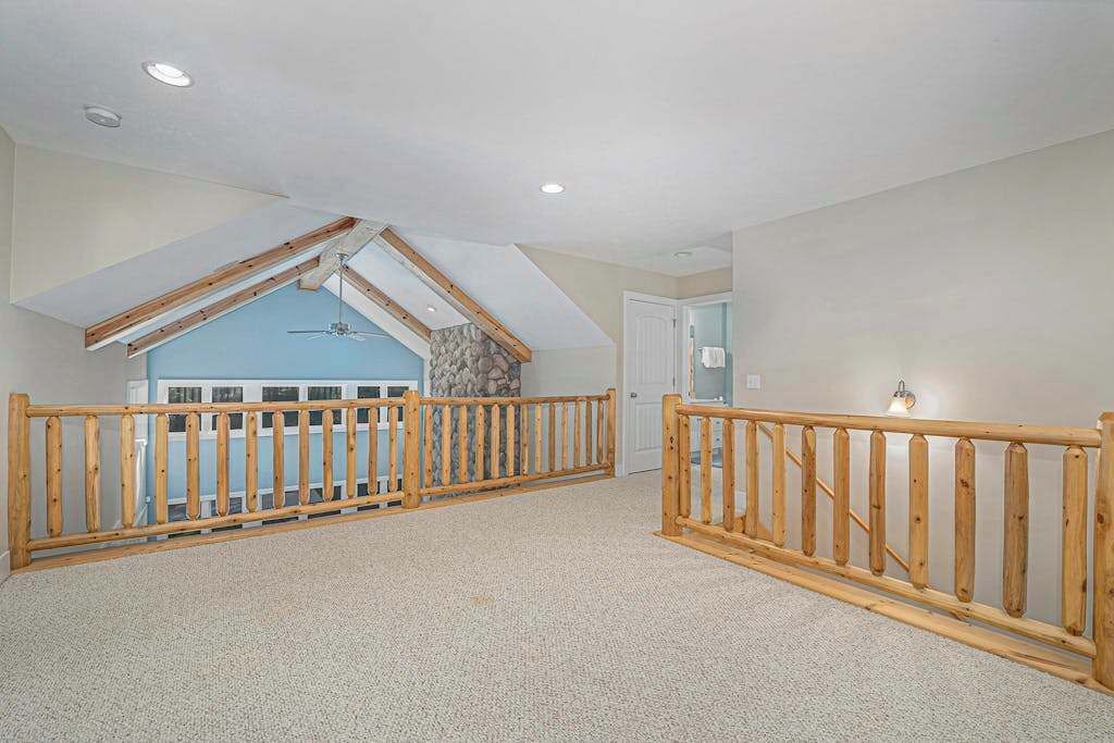 A spacious attic bedroom with a sloped ceiling, wooden railings, and a stone accent wall.