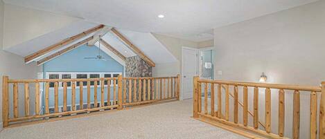 A spacious attic bedroom with a sloped ceiling, wooden railings, and a stone accent wall.