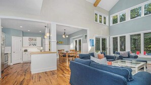Een ruime woonkamer met een blauwe bank, een glazen salontafel en een houten eettafel.