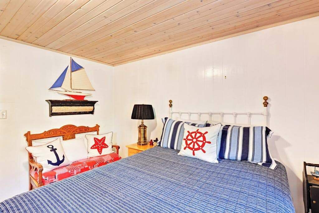 A bedroom with a wooden ceiling, a bed with striped bedding, a sailboat decoration, and a ship wheel pillow.
