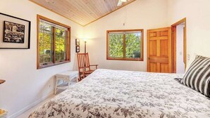 Ein Schlafzimmer mit einem Bett, zwei Fenstern, einem Deckenventilator, einer Tür und einem Stuhl.