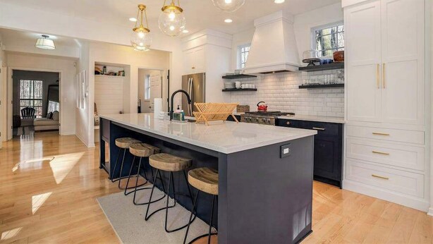 A modern kitchen with a central island, bar stools, pendant lighting, and white cabinetry.