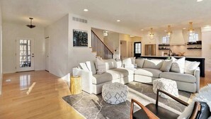 A spacious living room with a large sofa set, a dining area with a wooden table, and a kitchen with modern appliances.