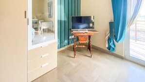 Una habitación con un armario, un televisor sobre un mueble de madera y una ventana con cortinas.