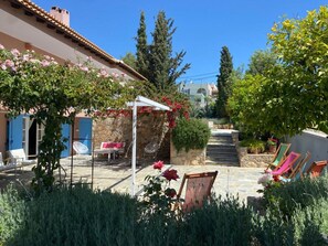 Ein Innenhof mit einem gepflasterten Weg, Außenmöbeln und einem Pergola, der mit blühenden Weinranken bewachsen ist.