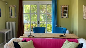 A room with a large window, a table with chairs, a sofa with cushions, and a radiator. - Villa-Agave, by the sea in Porto-Rafti outside ATH (Porto Rafti)
