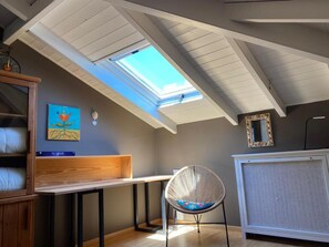 Ein Zimmer mit schrägem Dach, einem Oberlicht, einem Bett, einem Sessel, einem Heizkörper und einem Bild an der Wand.
