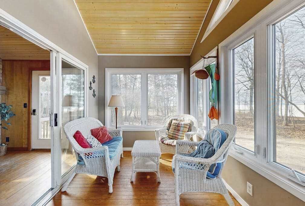 A room with wicker furniture, a wooden ceiling, and large windows.