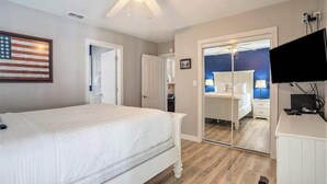 Un dormitorio con cama, ventilador de techo, televisor y puerta que da a otra habitación.