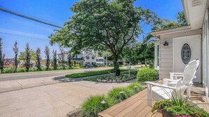 Una propiedad residencial con terraza de madera, mobiliario exterior, un árbol grande y un césped bien cuidado.