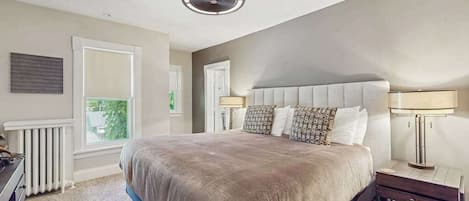 A bedroom with a large bed, a ceiling fan, a radiator, and a window.