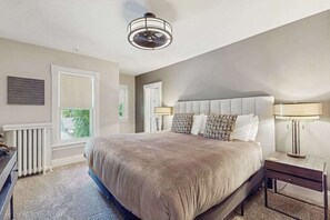 A bedroom with a large bed, a ceiling fan, a radiator, and a window. - Charming historical home with gated entrance & gas grill - walk around downtown (Saugatuck)