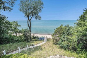 A beach with a pathway leading to a sandy area, surrounded by greenery and a clear view of the sea. - Lakefront Home w/High-Speed WiFi, Private Beach, Gas Grill, Washer/Dryer, & more (Harbert)