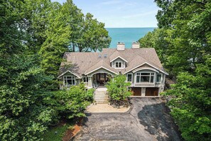 A large house with a driveway, surrounded by trees, and a view of the ocean. - Lakefront Home w/High-Speed WiFi, Private Beach, Gas Grill, Washer/Dryer, & more (Harbert)