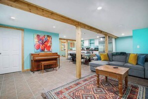 A spacious living area with a piano, a sofa, a coffee table, and a kitchen in the background. - Exclusive beach access, serene views, and family-friendly amenities (Coloma)