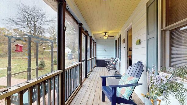 Eine überdachte Veranda mit Deckenventilator, Holzgeländer und Blick auf einen Garten mit einem roten Vogelhaus.