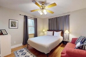 A bedroom with a bed, a ceiling fan, a nightstand, a lamp, a couch, a rug, and a window with curtains. - Within walking distance to Lake Michigan, beach access, nice patio, W/D & WIFI (Lakeside)