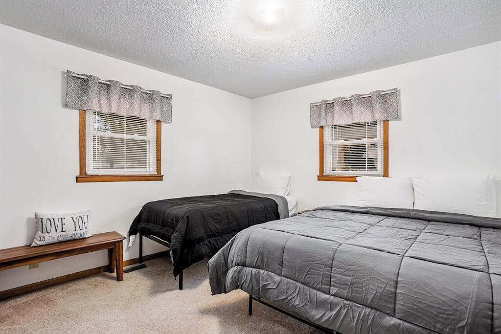Une chambre avec deux lits, un banc et un luminaire fixé au mur.