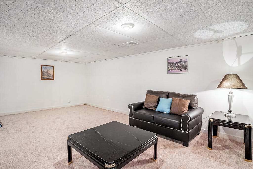 Et værelse med en sort lædersofa, et sort sofabord, en lampe og et indrammet billede på væggen.