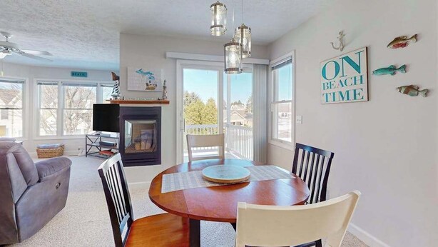 A dining area with a round table, chairs, a fireplace, and a view of the outside. - Charming 3 story condo, w/ a W/D & Wifi, near beaches & shared pool access (Manistee)