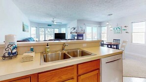 A kitchen with a double sink, wooden cabinets, a dishwasher, and a dining area with a table and chairs. - Charming 3 story condo, w/ a W/D & Wifi, near beaches & shared pool access (Manistee)