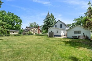 A residential area with houses, a large grassy yard, and a tall evergreen tree. - Updated, charming home with huge yard, fire pit, & WiFi - walkable location (South Haven)
