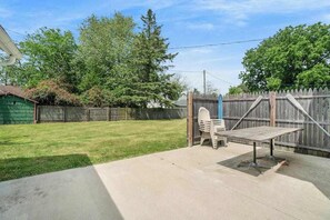 A backyard with a concrete patio, a wooden table, and a chair. - Updated, charming home with huge yard, fire pit, & WiFi - walkable location (South Haven)