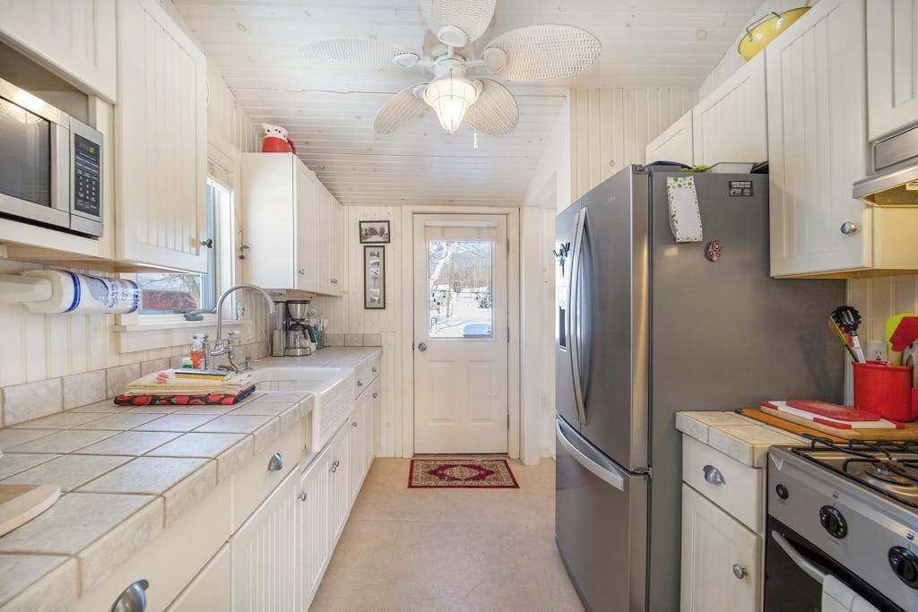 Una cocina compacta con muebles blancos, un refrigerador de acero inoxidable, una estufa a gas y un ventilador de techo.